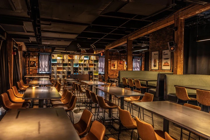 Warmly lit Trillium event room with long tables, booths, and brick walls.